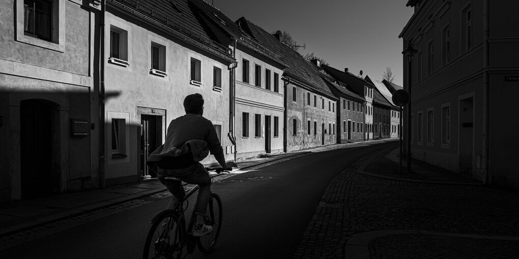 Eine Person auf einen Fahrrad vor Hausfassaden.