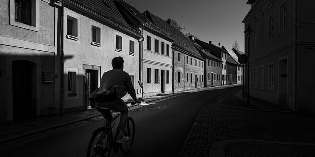 Eine Person auf einen Fahrrad vor Hausfassaden.
