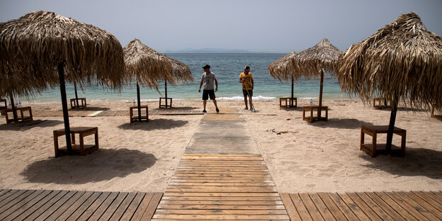 Zwei arbeiter an einem leeren Strand mit Sonnenschirmen und Liegen aus Holz