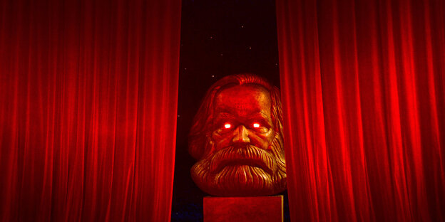 Büste eines bärtigen Mannes mit leuchtenden Augen vor einem roten Theatervorhang