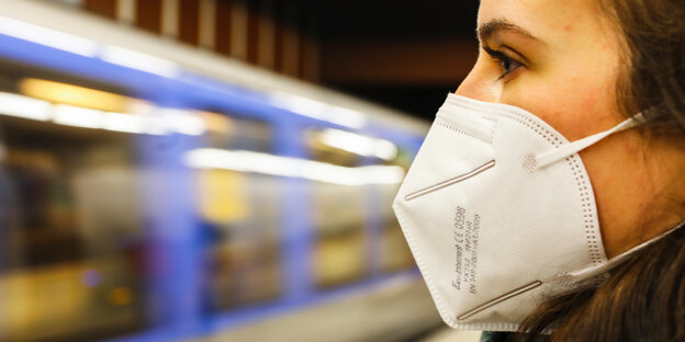 Eine Frau mit FFP2 Maske auf dem Gesicht steht an einer U-Bahn-Station in München. Die Bahn (eine der neueren, schicken) fährt gerade ein.