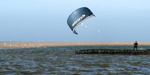 Ein Kitesurfer rast über die Nordseewellen vor dem Strand von Norderney.