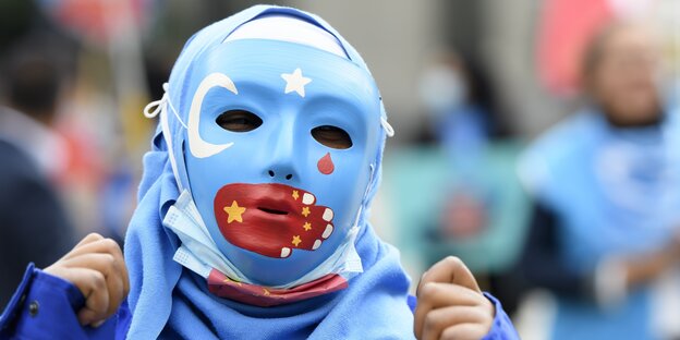 Maske mit Fahne der Uiguren, Mund mit chinesischer Fahne verschlossen