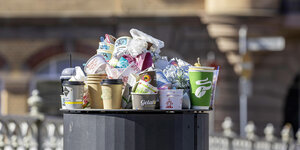 Müllberg mit Einwegbechern stapelt sich auf eine öffentlichen Mülltonne