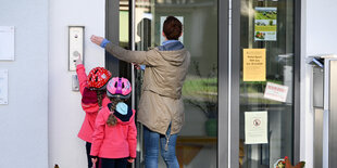 Eine Mutter steht mit ihren Kindern vor dem Kita-Eingang und klingelt.