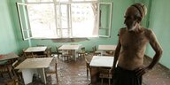 Mann mit nacktem Oberkörper schaut auf Glassplitter in einem Kindergarten