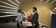 Balram (Adarsh Gourav, links) nimmt von Ashok (Rajkummar Rao) vor einem Auto eine edle Ledertasche entgegen.