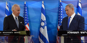 Joe Biden und Benjamin Netanjahu stehen sich bei einem Treffen nebeneinander an zwei Rednerpulten und unterhalten sich - Im Hintergrund US- und Israel Flaggen