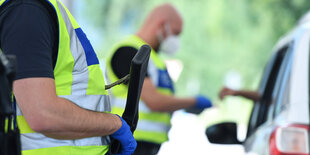 Ein Polizist kontrolliert den Fahrer eines PKWs - ein weiterer Steht mit Maschinengewehr daneben