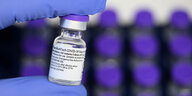 Eine Person mit Gummihandschuh hält ein Fläschchen Impf-Serum