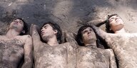 Vier junge Männer liegen nackt im Sand