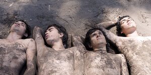 Vier junge Männer liegen nackt im Sand