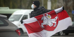 Ein Mann mit Mund-Nasen-Schutz hält eine weiß-rot-weiße Flagge der belarussischen Opposition