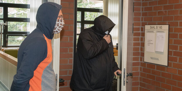 Zwei mit Kapuze und Mundschutz vermummte Männer stehen vor einem Gerichtssaal im Amtsgericht Tiergarten. Sie sind nicht zu erkennen.