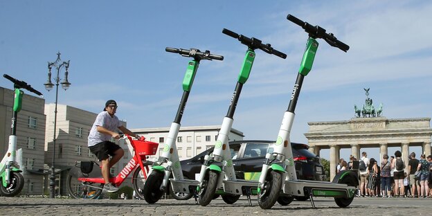 Drei grünweiße E-Roller zum Ausleihen stehen in einer Reihe vor dem Brandenburger Tor
