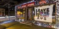 EIn mit Auklebern und Graffiti übersähter Club unter der Sternbrücke, im Fenster ein Plakat mit der Aufschrift "Leave no one behind"