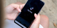 Zwei Hände halten ein Smartphone, auf dem Display sieht man das Logo von Tiktok