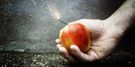 Eine Hand hält einen Apfel mit Zündschnur