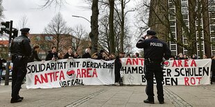 Jugendliche mit Antifa-Transparent hinter zwei Polizisten