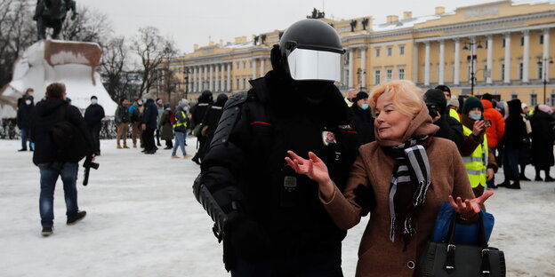 Ein vermummter Polizist führt eine ältere Dame ab