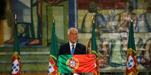 Ein älterer Herr hinter einem mit der portugiesischen Flagge geschmücktem Rednerpult