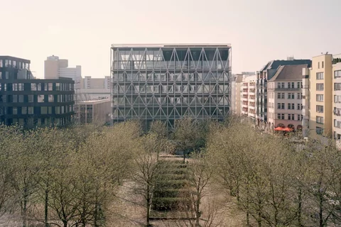 Ein Panoramablick auf den taz Neubau, im Vordergrund stehen die vielen Kastanienbäume des Kreuzberger Besselparks im noch zarten Grün