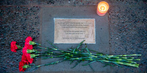 Blumen liegen und eine Kerze liegen neben einer Gedenkplatte auf dem Boden bei einer Kundgebung von linken Gruppen gegen Polizeigewalt vor dem Eingang des Hauses, in dem Maria B. getötet wurde – vor genau einem Jahr