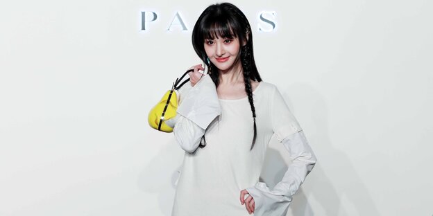 Zheng Shuang eine junge chinesische Schaupielerin posiert vor weißem Hintergrund und trägt eine kleine gelbe Handtasche