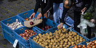 Menschen suchen sich Kartoffeln und Zwiebeln auf einem Lebensmittelmarkt aus