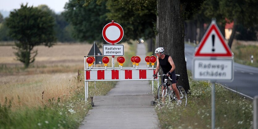 Schäden an einem Radweg an der Bundesstraße 3- Ein Radfahrer muss um die Absperrung schieben