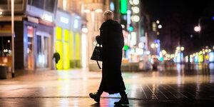 Eine junge Frau geht alleine durch eine beleuchtete Fussgängerzone