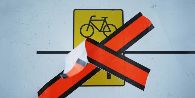 Ein mit orangen Klebeband durchgestrichenes Schild mit einem fahrrad-Symbol