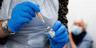 Eiine medizinische Mitarbeiterin mit blauen Handschuhen zieht eine Spritze mit dem Serum auf