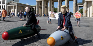 Zwei als US-Präsident Trump und als russischer Präsident Putin verkleidete Aktivisten fahren vor dem Brandenburger Tor während einer Demo für eine Welt ohne Atomwaffen auf zwei Modellen von Atombomben