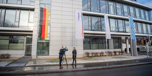 Journalisten mit Mikrofon und Kamera vor einem Firmengebäude mit Deutschlandfahne