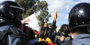 Ein Brot wird von Demonstranten in die Höhe gehalten, Polizeihelme im Vordergrund