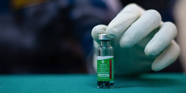 Eine Ampulle AstraZeneca-Corona-Impfstoff AZD1222 und die Hand einer medizinischen Fachkraft mit Schutzhandschuhen