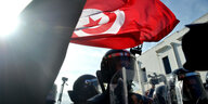 Ein Demonstrant mit der Flagge von Tunesien und Polizisten