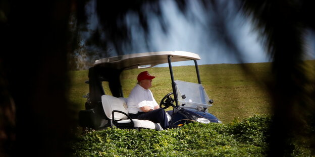 Donald Trump in einem Golfwägelchen hinter Palmen