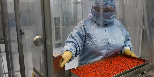 Eine Arbeiterin mit voller Schutzmontur verpackt Impfdosen