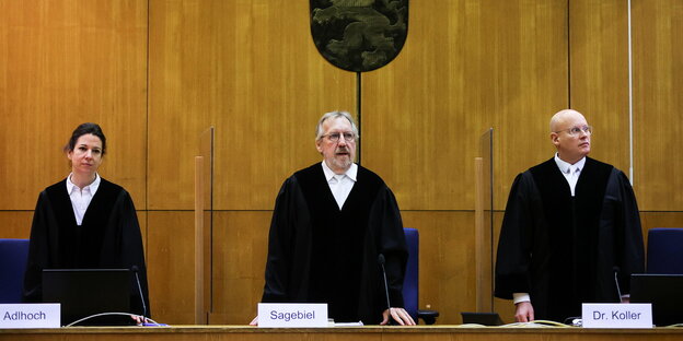 Drei RichterInnen in Robe stehen im Gerichtssaal