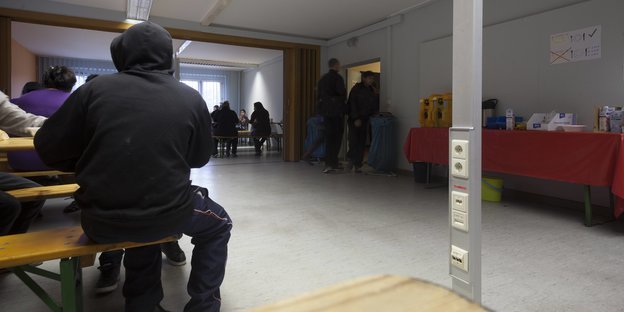 Flüchtlinge sitzen in einem kargen Wartesaal in einer Notunterkunft in Berlin_Grünau.