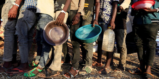 Äthiopischen Flüchtlingen stehen mi Schüsseln in der Hand bei einer Essensausgabe an.