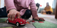 Kleinkind spielt mit einem roten Spielzeugauto auf dem Teppich
