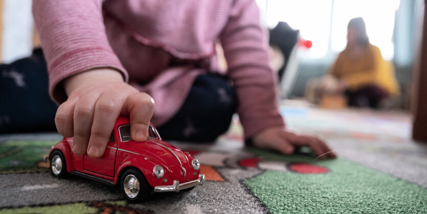 Kleinkind spielt mit einem roten Spielzeugauto auf dem Teppich