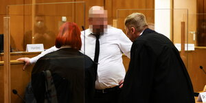 Ein Mann mit dickem Bauch und weissem Hemd spricht mit zwei Anwältinnen in Robe