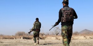 Zwei Soldaten mit Waffen patrouillieren in karger Landschaft