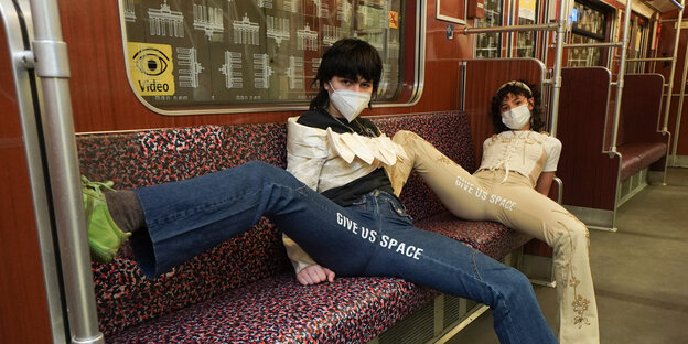 Designer*innen Mina Bonakdar und Elena Buscaino zeigen ihre Hosen mit gespreizten Beinen in der Berliner U-Bahn