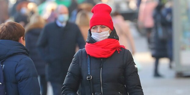 Eine Frau trögt eine rote Mütze, einen roten Schal und einen weißen Mundschutz