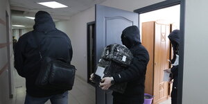 Vermummte Einsatzkräfte tragen Gegenstände aus einem Büro